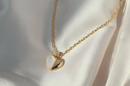 Gold necklace with a heart-shaped pendant on a white fabric background