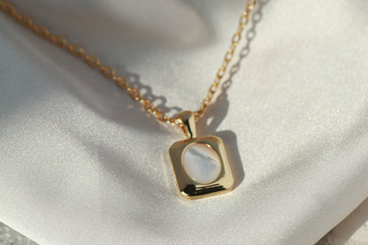 Gold necklace with a square pendant on a white fabric background