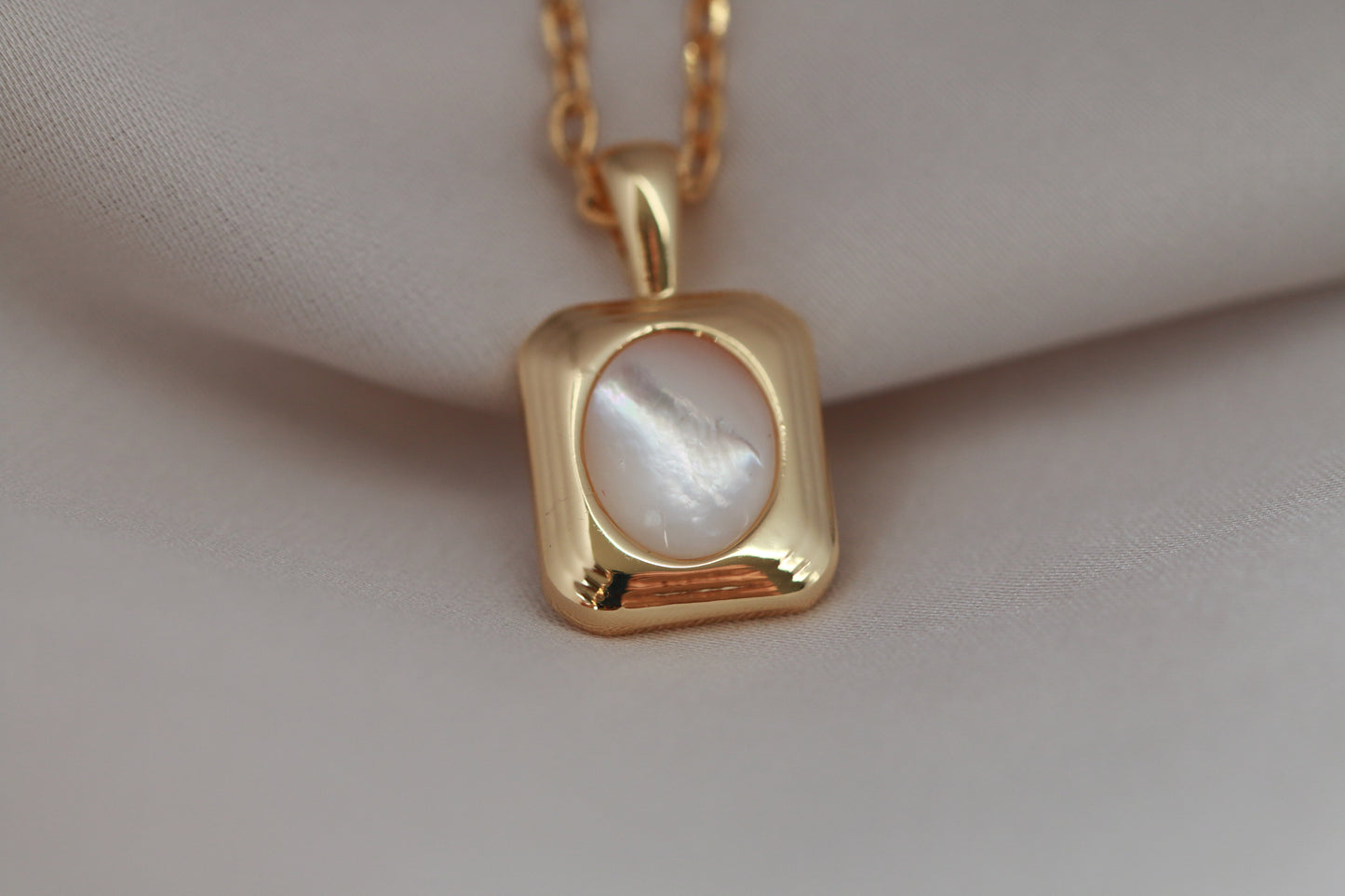 Gold necklace with a pendant on a beige fabric background