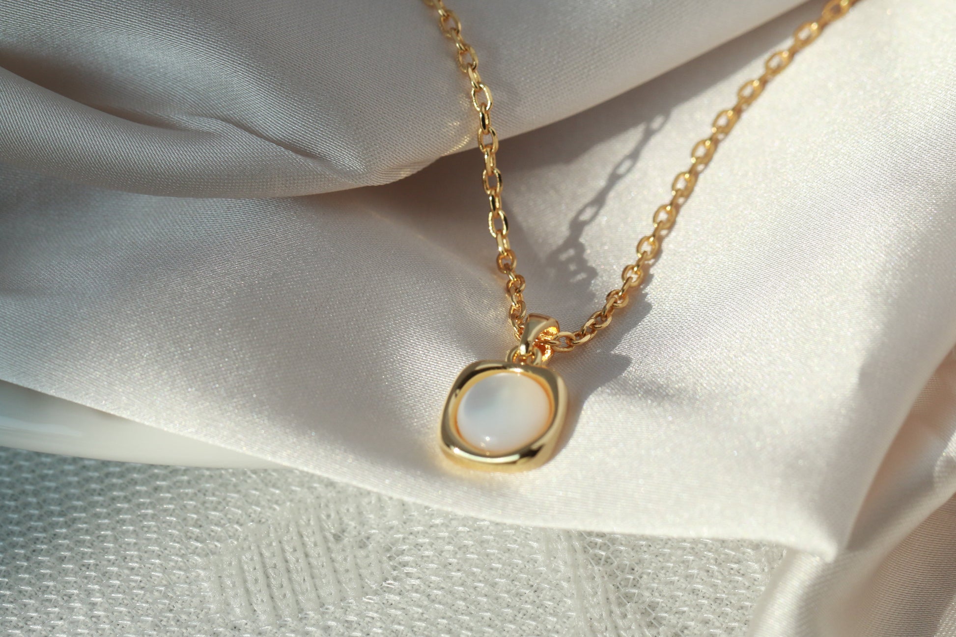 Gold necklace with a round pendant on a white fabric background