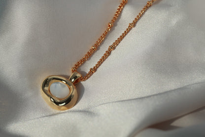 Gold necklace with a circular pendant on a white fabric background