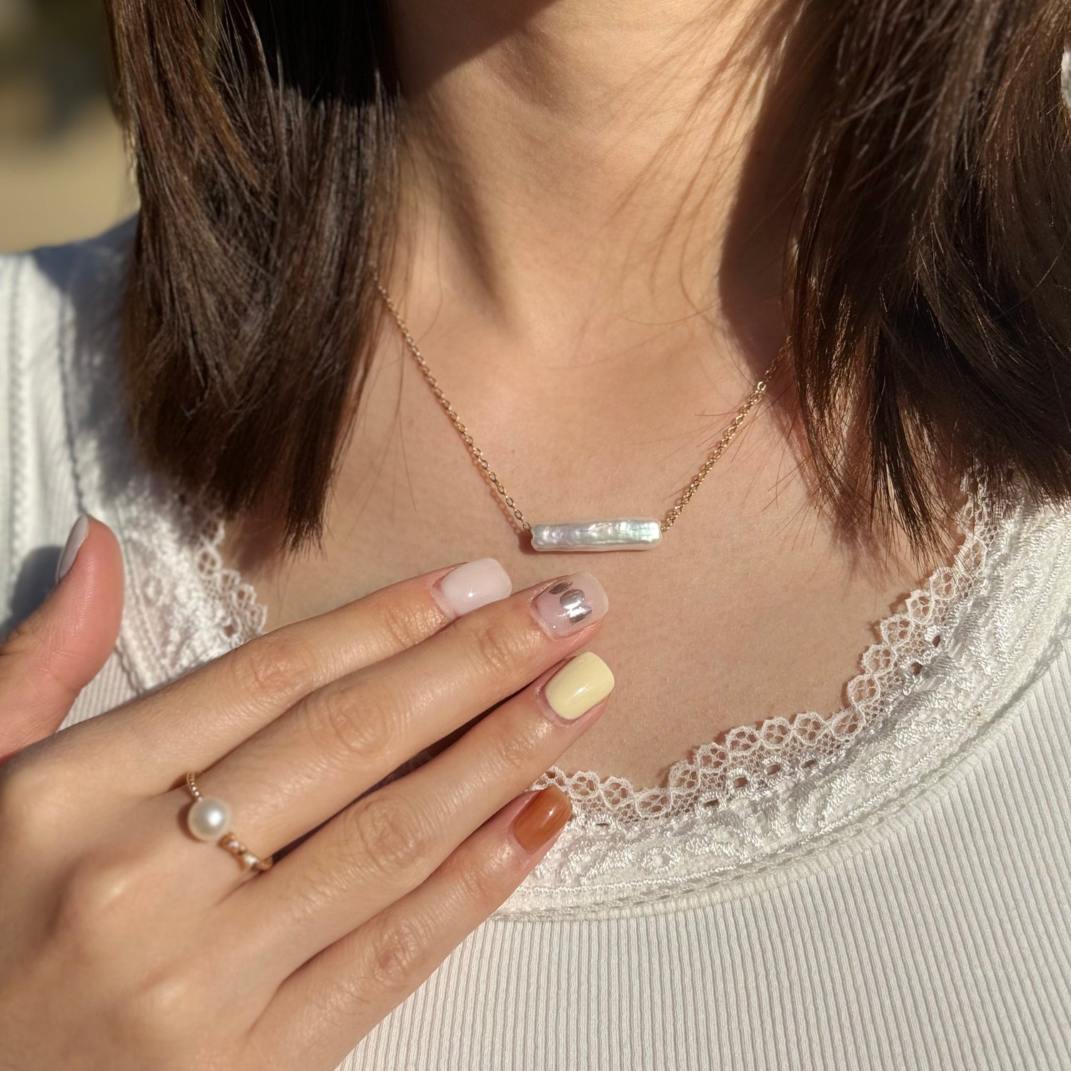Person wearing a necklace with a bar pendant and a ring on a white lace top.
